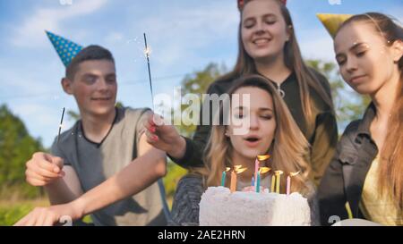 Happy amici celebrano la loro ragazza il compleanno. La ragazza di compleanno si brucia le candele. Foto Stock