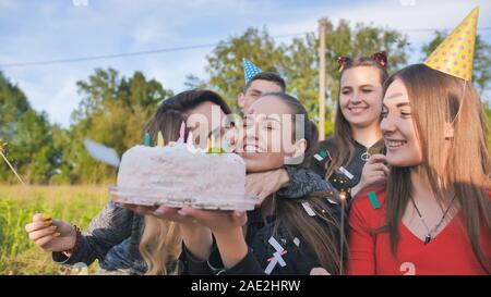 Happy amici celebrano la loro ragazza il compleanno. La ragazza di compleanno si brucia le candele. Foto Stock