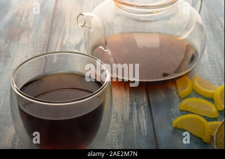 La marmellata di arance fette di limone, un bicchiere di tè nero e una teiera con infuso di tè su un sfondo di legno. Dolce con. Close up Foto Stock