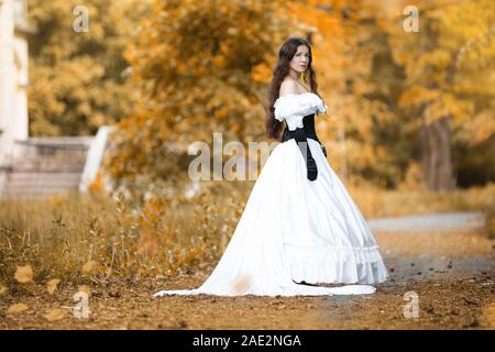 La donna in un bianco abito vittoriano in un parco di autunno