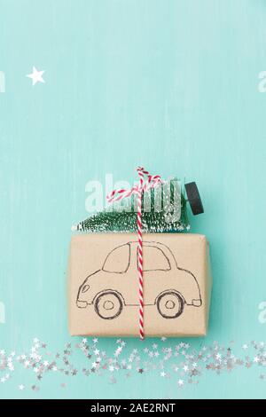 Vista dall'alto sul regalo di Natale avvolto in artigianato carta regalo decorata con disegno auto con albero di Natale sul turchese sullo sfondo di legno con spumante st Foto Stock