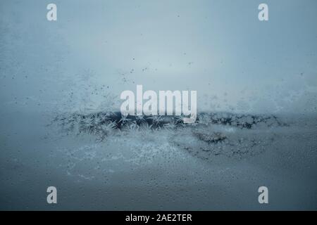 Congelati finestra con vetro frosty pattern e grigio scuro paesaggio invernale sfocati in background Foto Stock