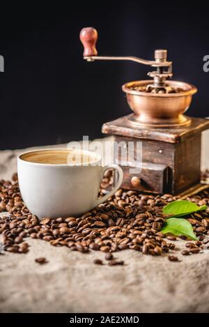 Una tazza di caffè con la schiuma e un di legno vintage macinino da caffè. Profumata bevanda rinvigorente da appena il caffè torrefatto in grani. Foto Stock