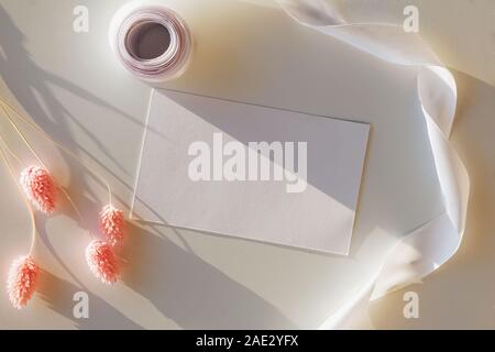 Svuotare la scheda Carta mock-up sul tavolo con fiori secchi e nastro nella luce solare naturale Foto Stock