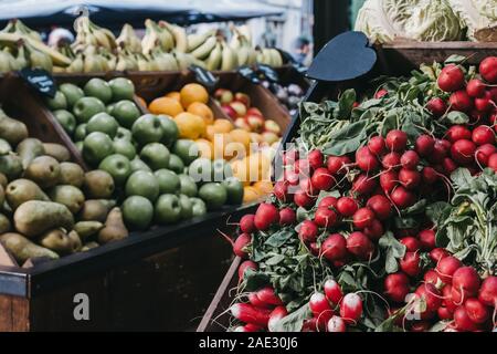 Mazzetti di ravanelli in vendita su un mercato in stallo, frutta in casse sullo sfondo, il fuoco selettivo. Foto Stock