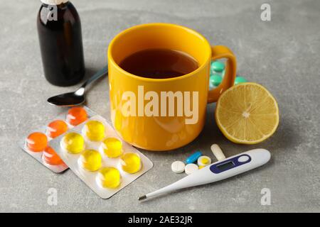 Composizione con diverse pillole, termometro, medico buttles, tazza di tè e caffè e limone su sfondo grigio. Vista superiore Foto Stock