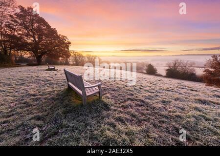 Panca di legno alla ricerca sulle Misty High Weald paesaggio coperto di brina in corrispondenza sunrise, Burwash, East Sussex, England, Regno Unito, Europa Foto Stock