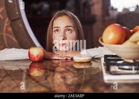 Rendere divertente faccia. Carino giovane massaia appoggiata sul tavolo con Apple e il cookie e guarda in alto Foto Stock