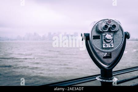 New York City mirino binocolo. Un tradizionale turistico mirino sulla Liberty Island guardando verso la skyline di New York su un grigio e nuvoloso giorno. Foto Stock