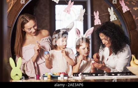 Nonna sta aiutando. Sono felice Pasqua. Due bambine imparare a dipingere le uova per le vacanze Foto Stock