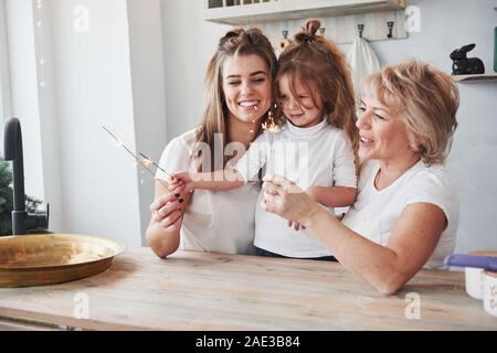 Luci di bengala nelle loro mani. Madre, la nonna e la figlia avente un buon tempo in cucina Foto Stock