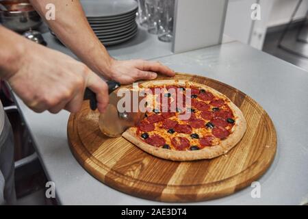 Per affettare a pezzi. Immagine del preparato una deliziosa pizza con anelli di salsiccia e olive Foto Stock