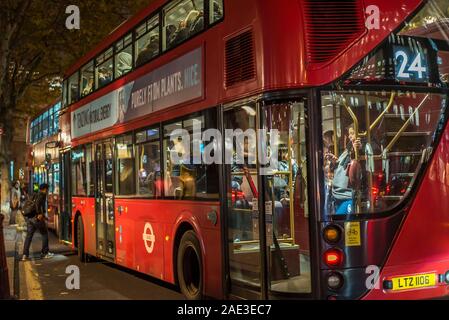 Vista laterale posteriore primo piano del grande autobus a due piani rosso di Londra di notte con passeggeri a bordo fermi al marciapiede. Trasporti pubblici di Londra. Foto Stock