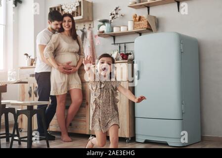 Gente allegra. Femmina giocoso bambino divertirsi eseguendo in cucina al giorno di fronte a lei il padre e la madre Foto Stock