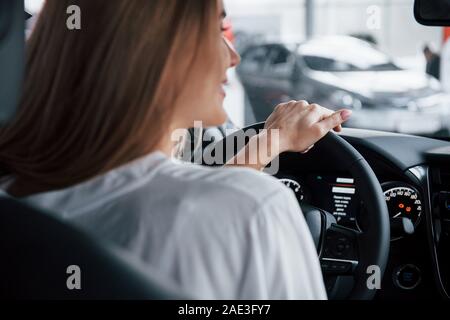 Equitazione e sorridente. Bella ragazza bionda seduta nella nuova vettura con i moderni interni neri Foto Stock