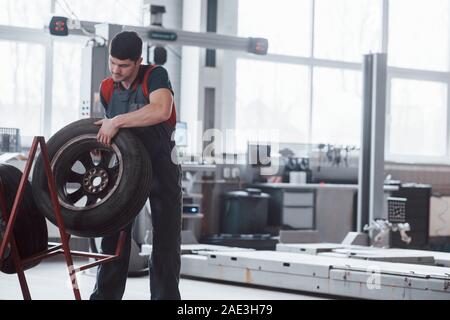 Mettere la ruota sul supporto. Mechanic tenendo un pneumatico in corrispondenza del garage di riparazione. Sostituzione delle gomme invernali ed estive Foto Stock