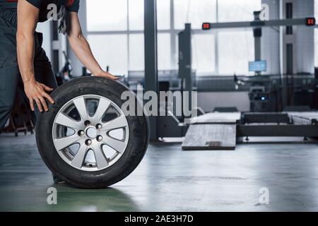 Vista dotata di messa a terra. Mechanic tenendo un pneumatico in corrispondenza del garage di riparazione. Sostituzione delle gomme invernali ed estive Foto Stock