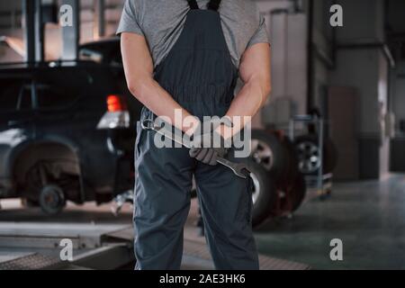 Mani muscolare. Vista posteriore del lavoratore in uniforme che si erge in officina con la chiave in mano Foto Stock