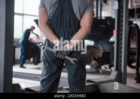 Vista posteriore del lavoratore in uniforme che si erge in officina con la chiave in mano Foto Stock