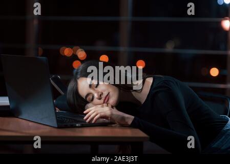 Dormire sul posto di lavoro. Attraente brunette imprenditrice si siede da solo in ufficio in notturna Foto Stock