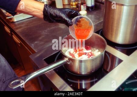 Coperta da un guanto chef è aggiunta messo a dura prova i pomodori in un piatto, cucina professionale, tonica foto Foto Stock