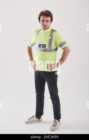 Un poliziotto in divisa verde si erge contro uno sfondo bianco in studio Foto Stock