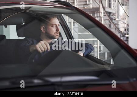 Guarda pensieroso. Vista frontale del giovane imprenditore barbuto seduto nel suo lusso auto rossa Foto Stock
