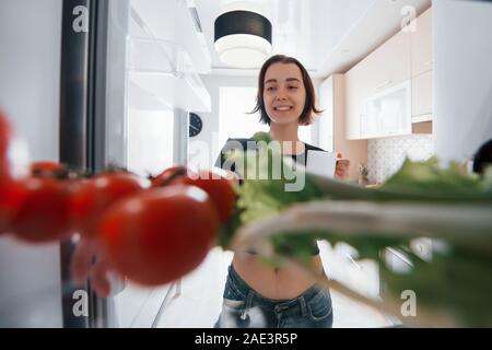 All'interno del frigorifero. Ragazza carina aprire la porta e a guardare cosa c'è all'interno di Foto Stock