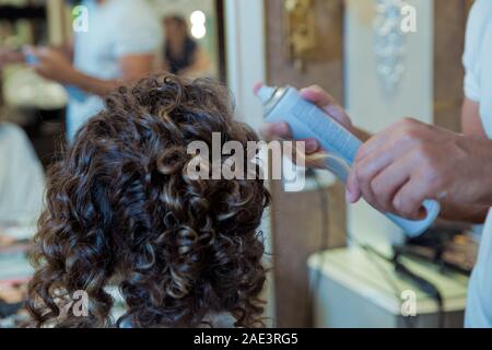 Parrucchiere è utilizzando un spray per capelli sulla donna capelli in un salone di bellezza su uno sfondo di colore marrone. Concetto di parrucchiere professionista studiando.bionda parrucchiere Foto Stock