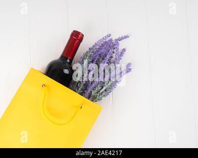 Bottiglia di vino in confezione con un dono, fiori su sfondo di legno, copia spazio, dono, vacanze, risalente, laici piatta Foto Stock