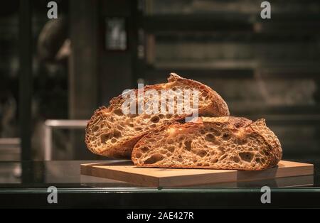 Pasta madre pane tagliato a metà su una tavola di legno, su un tavolo. Bakery Shop contesto. Deliziosa pagnotta di pane di pasta acida. Il tedesco il pane appena sfornato. Foto Stock