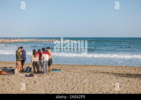 Un gruppo di adolescenti in spiaggia per guardare i surfisti e surf sulle onde alte, mare mosso, Fuengirola, Andalusia, Spagna Foto Stock