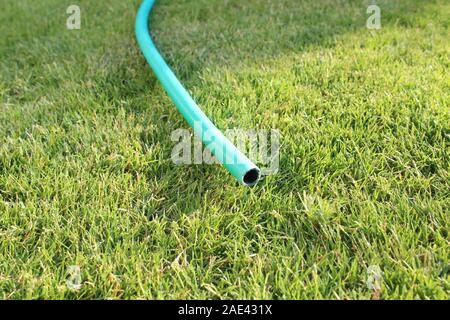 Close up di un verde acqua in plastica flessibile con senza acqua corrente che giace un po' piegate, sul verde a breve il taglio di erba. Foto Stock