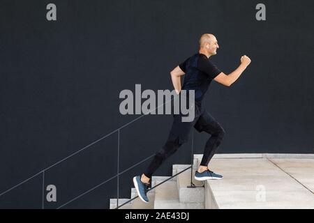 Giovani alto uomo virile è attivo nello sport sulla strada contro un muro nero lo sfondo Foto Stock