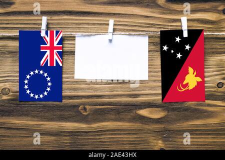 Appendere bandiere delle Isole Cook e Papua Nuova Guinea attaccata alla corda con vestiti perni con copia spazio bianco sulla nota carta su sfondo di legno.Diploma Foto Stock