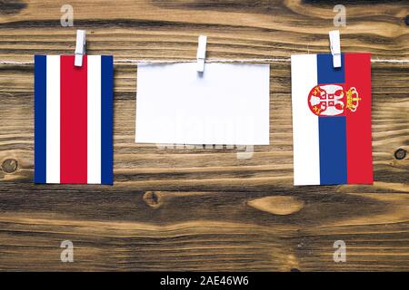 Appendere bandiere di Costa Rica e la Serbia attaccata alla corda con vestiti perni con copia spazio bianco sulla nota carta su sfondo di legno.Relazione Diplomatica Foto Stock