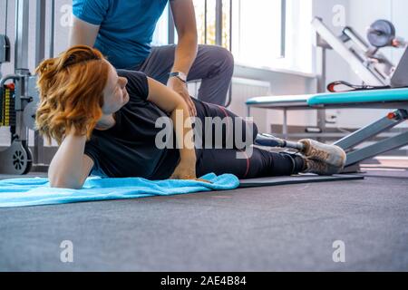 Personal trainer assiste la donna con disabilità nel suo allenamento. Sport centro riabilitativo con fisioterapisti e pazienti che lavorano insieme verso hea Foto Stock