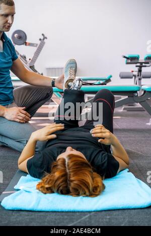 Personal trainer assiste la donna con disabilità nel suo allenamento. Sport centro riabilitativo con fisioterapisti e pazienti che lavorano insieme verso hea Foto Stock