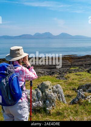 Donna vacanzieri in cerca attraverso il binocolo da Colonsay attraverso il mare per le pappe del Giura, Ebridi Interne, Scotland, Regno Unito Foto Stock