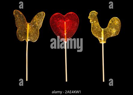 Dolce zucchero caramellato lecca-lecca isolati su sfondo nero a forma di farfalla cuore rosso galletto close-up Foto Stock