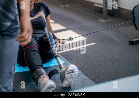 Personal trainer assiste la donna con disabilità nel suo allenamento. Sport centro riabilitativo con fisioterapisti e pazienti che lavorano insieme verso hea Foto Stock