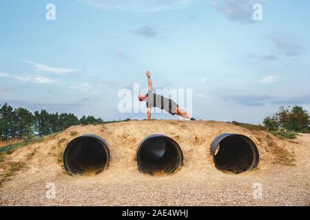 Montare un uomo si estende il suo braccio al cielo blu in un yoga pone su una collina Foto Stock