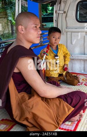 Un giovane monaco buddista e un ragazzino con un coltello di plastica sedere su un tappeto nel retro di un bus jitney in attesa di discostarsi in Mandalay, Myanmar (Birmania) Foto Stock