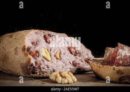 Filone di pasta madre francese, chiamato anche Pain de campagne, ripiene di carne e noci su uno sfondo nero con una fetta di pane con salsiccia secca ( Foto Stock