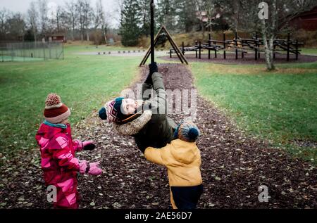 La madre a giocare con i suoi bambini al parco giocando su uno swing Foto Stock