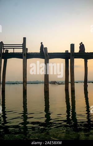 I monaci buddisti si stagliano dal sunrise come essi a piedi attraverso gli antichi di legno di teak U Bein ponte attraverso il lago Taungthaman ad Amarapura, nei pressi della città di Mandalay in Myanmar (chiamato in precedenza Foto Stock