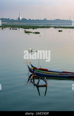 Sunrise vista di una barca vicino all'antico legno di teak U Bein ponte che si estende attraverso il lago Taungthaman ad Amarapura, nei pressi della città di Mandalay in Myanmar (ex Birmania chiamato) Foto Stock