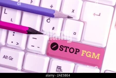 La grafia la scrittura di testo Stop fgm. Foto concettuale di porre fine o di arresto sul taglio genitale e la circoncisione White tastiera PC con nota vuota abo della carta Foto Stock