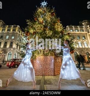 Londra, Regno Unito. 6 dicembre, 2019. Danzatori provenienti da un semaforo della Compagnia di Balletto eseguire in fairy illuminato abiti leggeri accanto a St James albero di Natale sul Lower Regent Street. Ballerini (L-R) Amy Davies e gelsomino Cook. Credito: Guy Corbishley/Alamy Live News Foto Stock