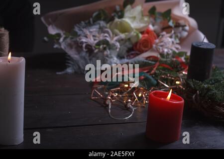 Close-up di un accogliente desktop di un fioraio con candele accese durante la creazione di una ghirlanda di Natale, il fuoco selettivo Foto Stock